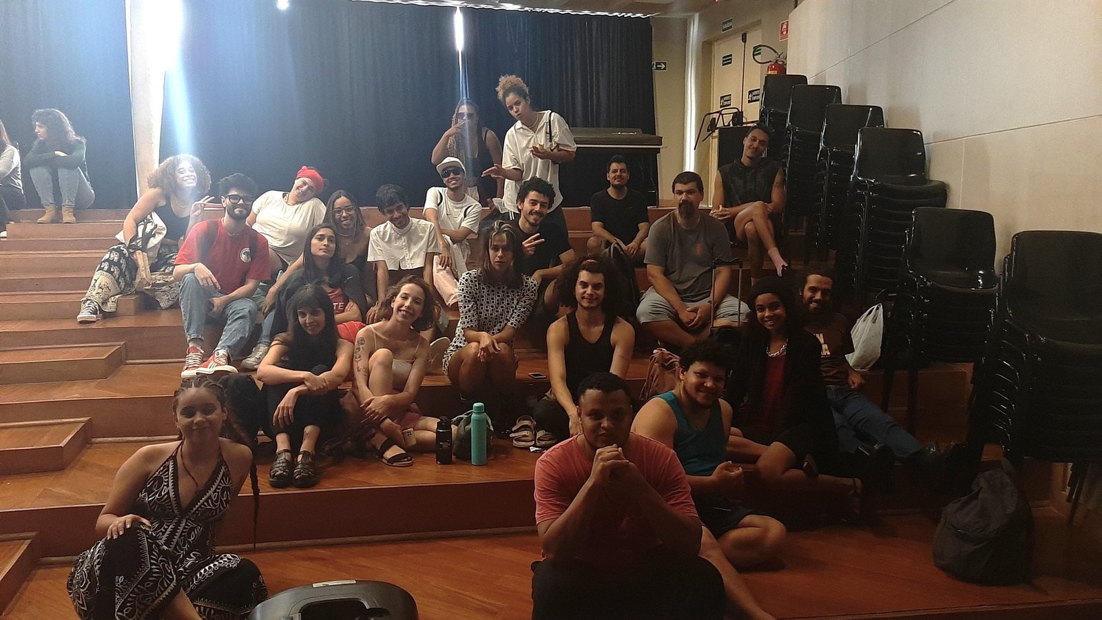 Foto colorida mostrando os estudantes da SP Escola de Teatro sentados no tablado do auditório da sede Brás