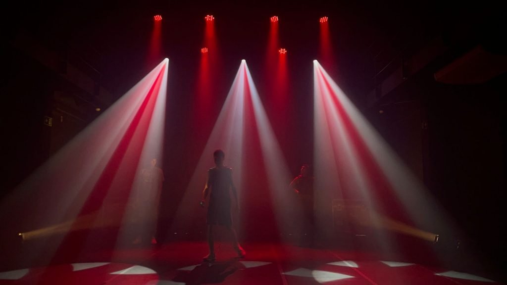 Foto mostrando a combinação da luz vermelha com a branca. Três estudantes da SP Escola de Teatro estão presente