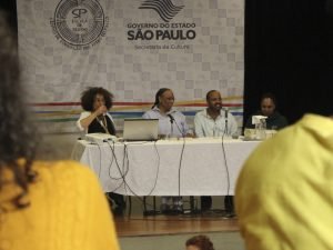 Fotografia colorida da mesa do evento formativo "Letramento Racial" composta por Isildinha, Tâmara, Miguel e Monica